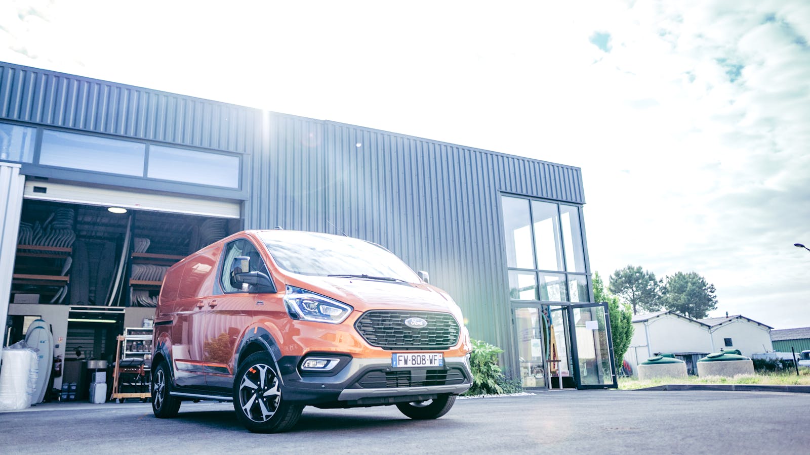 Low angle shot of an orange Ford Tourneo van parked outside a modern industrial building.